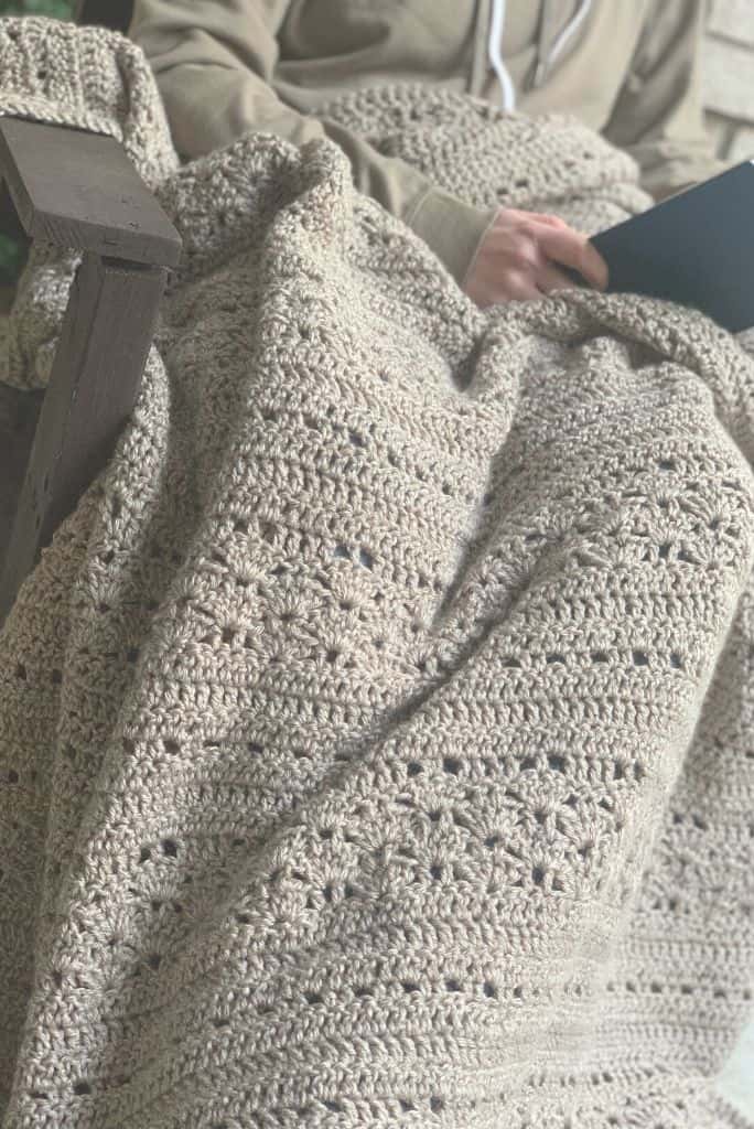 person sitting in chair with blanket, reading a book