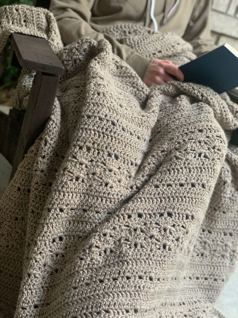 person sitting in chair reading a book with a blanket on their lap