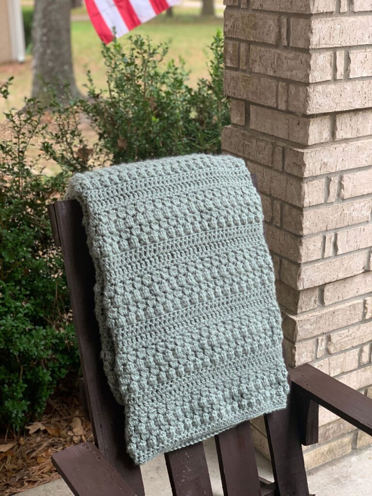 crochet throw blanket thrown over back of outdoor chair on front porch
