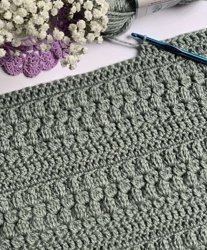 crochet blanket with hook, skein of yarn, and decorate flowers
