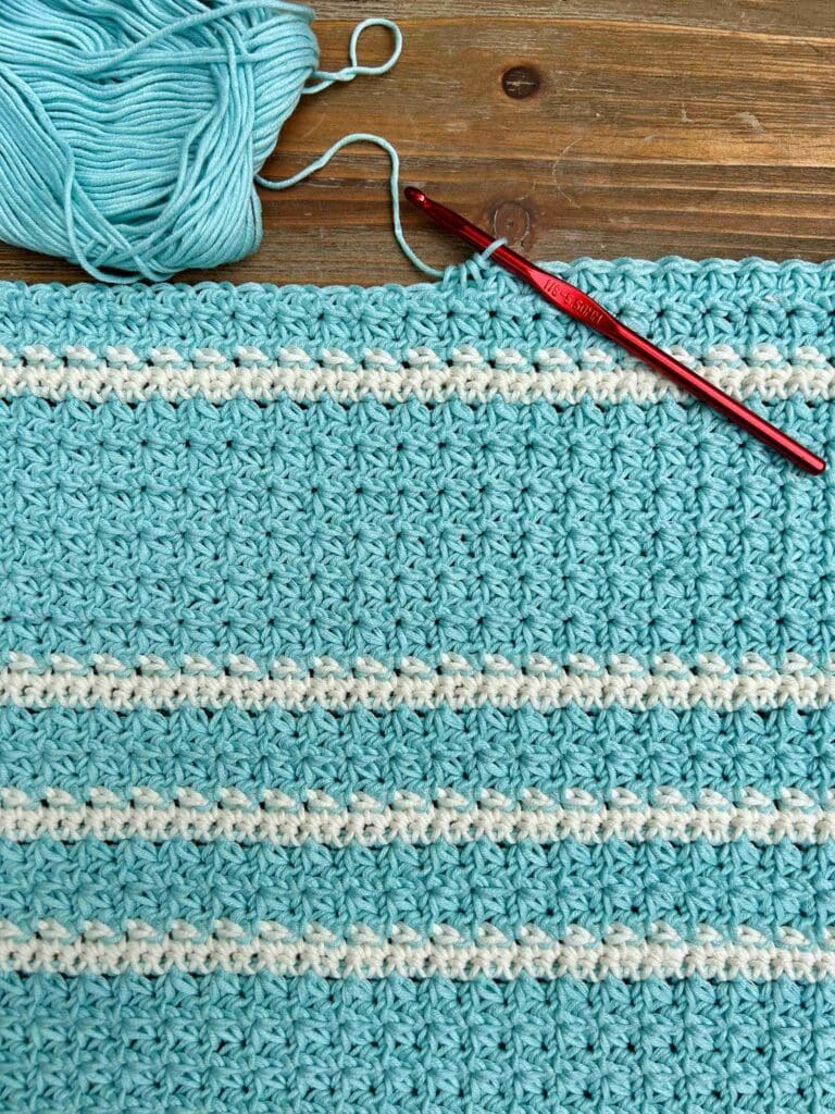 blue and white crochet project with red crochet hook