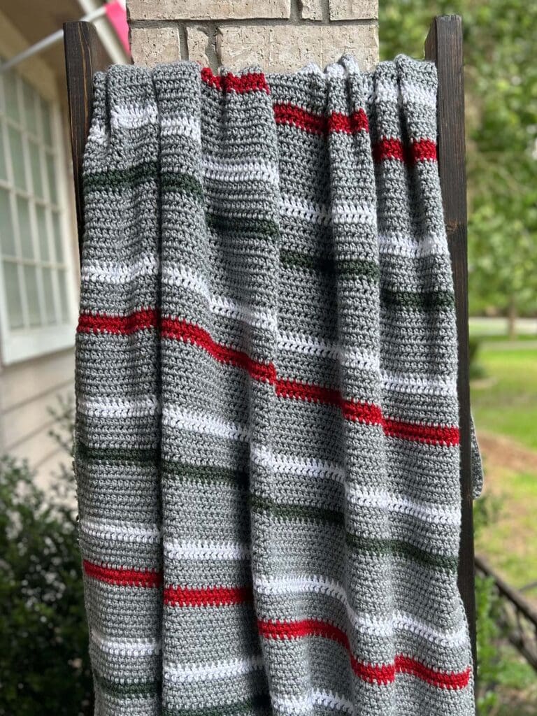 Gray throw blanket with red, green, and white stripes on blanket ladder
