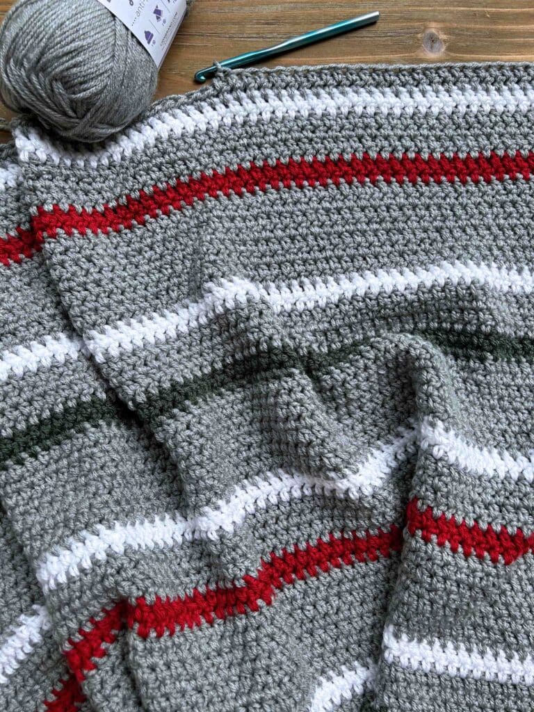 gray, white, red, and green crochet project with crochet hook and yarn