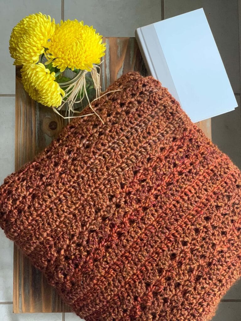 orange throw blanket on an end table with yellow flowers and a hardback book