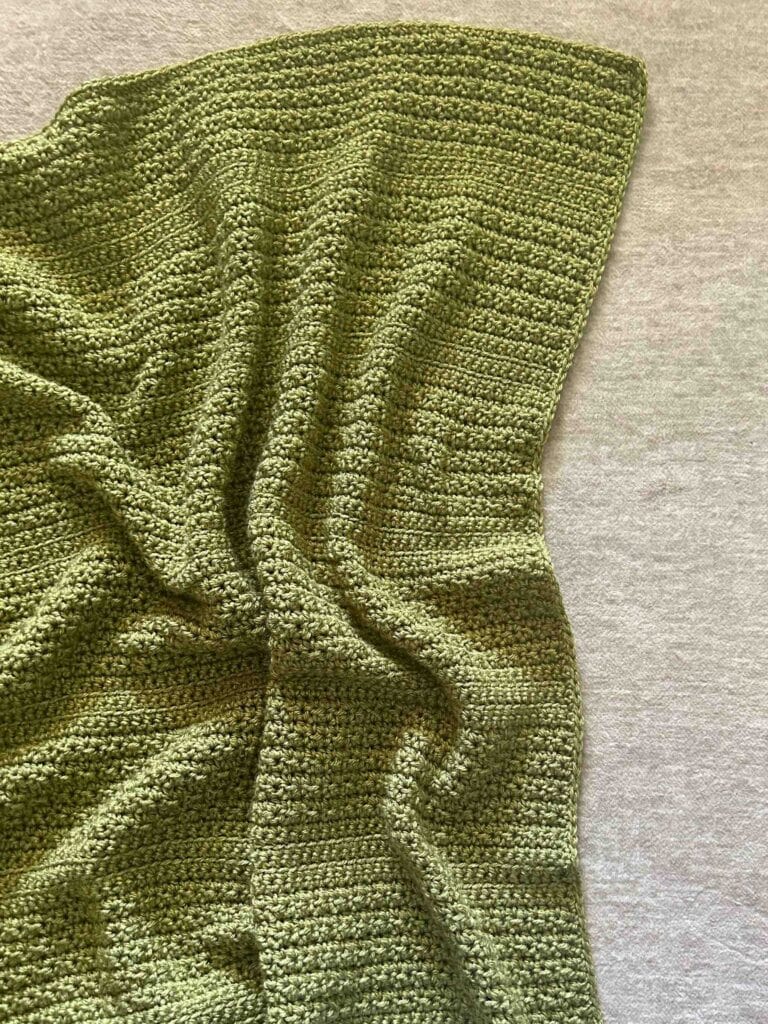 green crochet baby blanket laid on soft surface