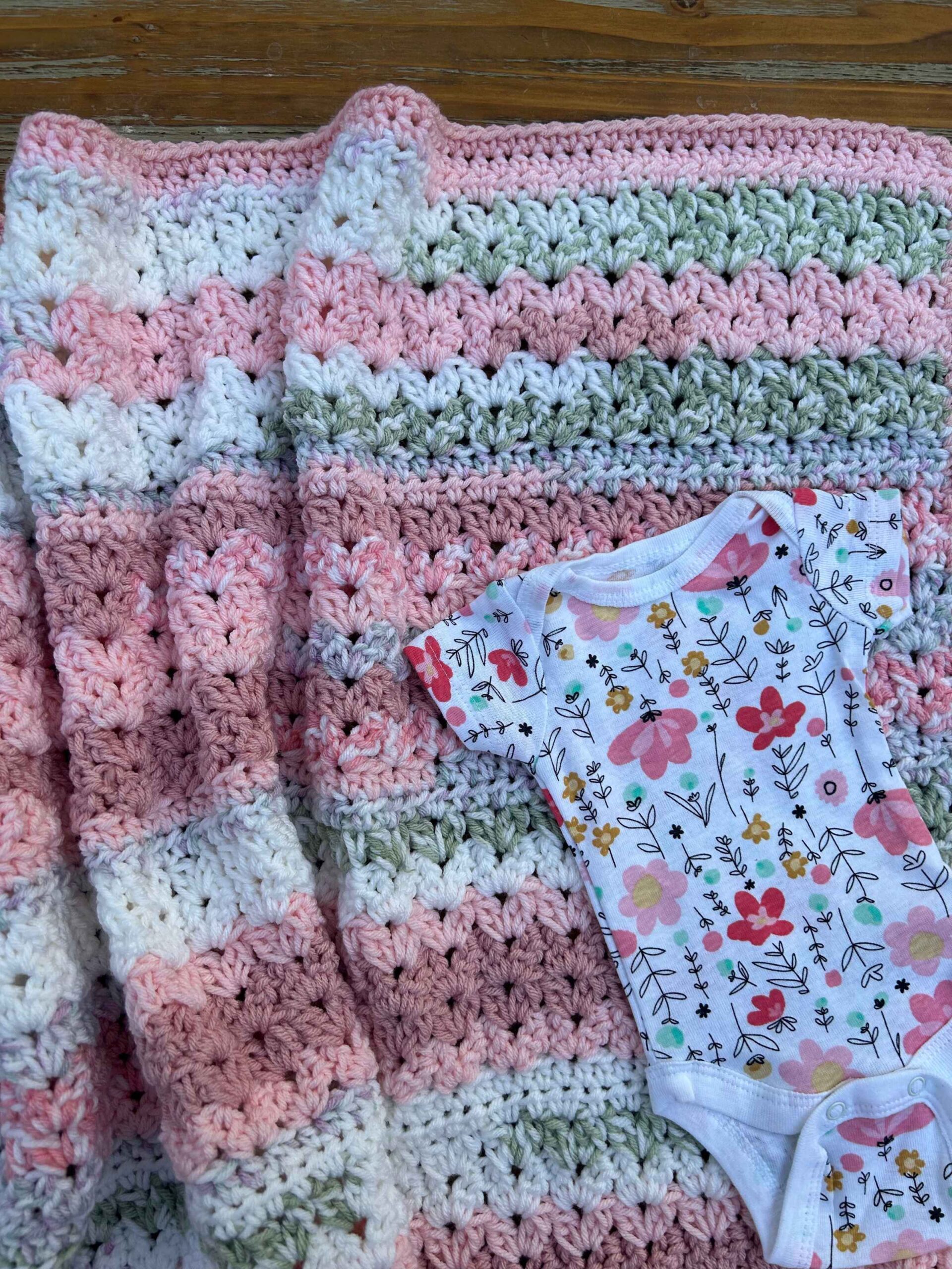 easy baby blanket crochet project with cluster v-stitches using pink, white, and green yarn with flowered baby outfit