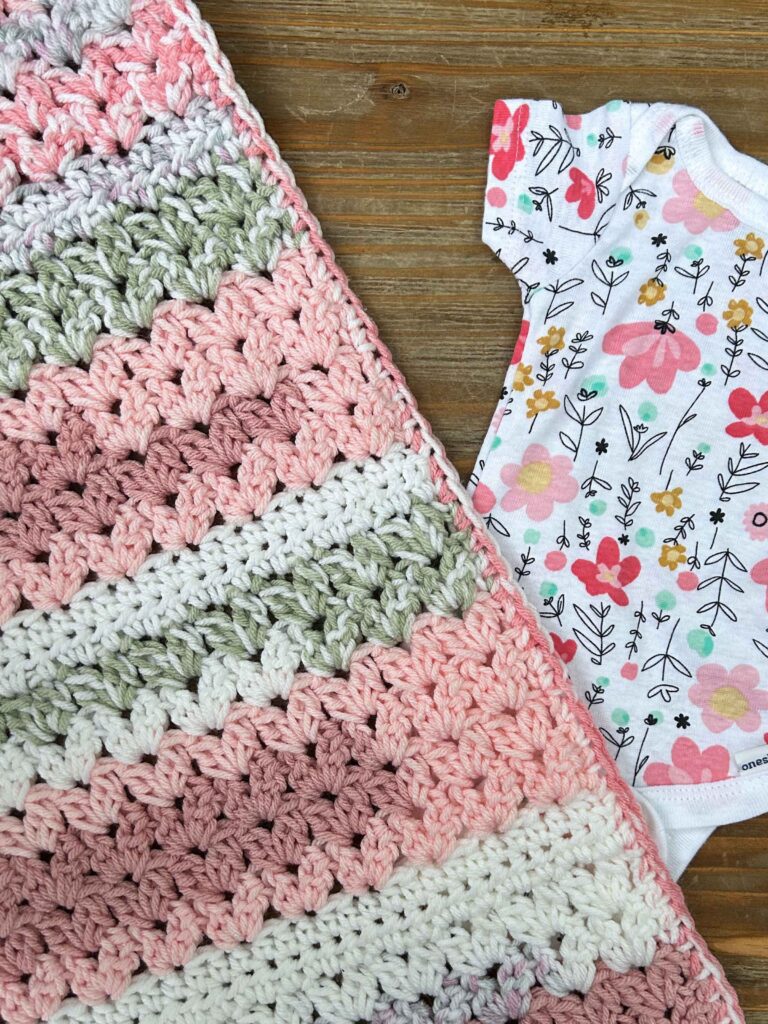 easy baby blanket crochet project with cluster v-stitches using pink, white, and green yarn with flowered baby outfit