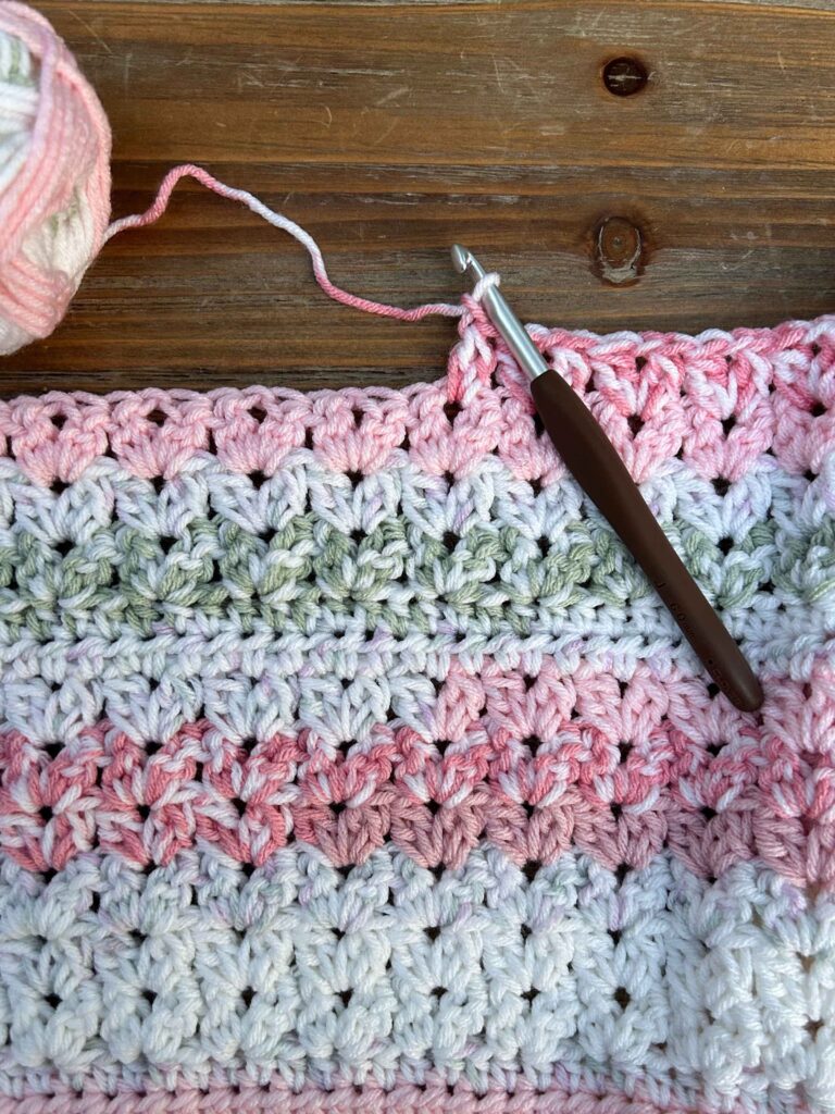 crochet project work in progress with cluster v-stitches using pink, white, and green yarn