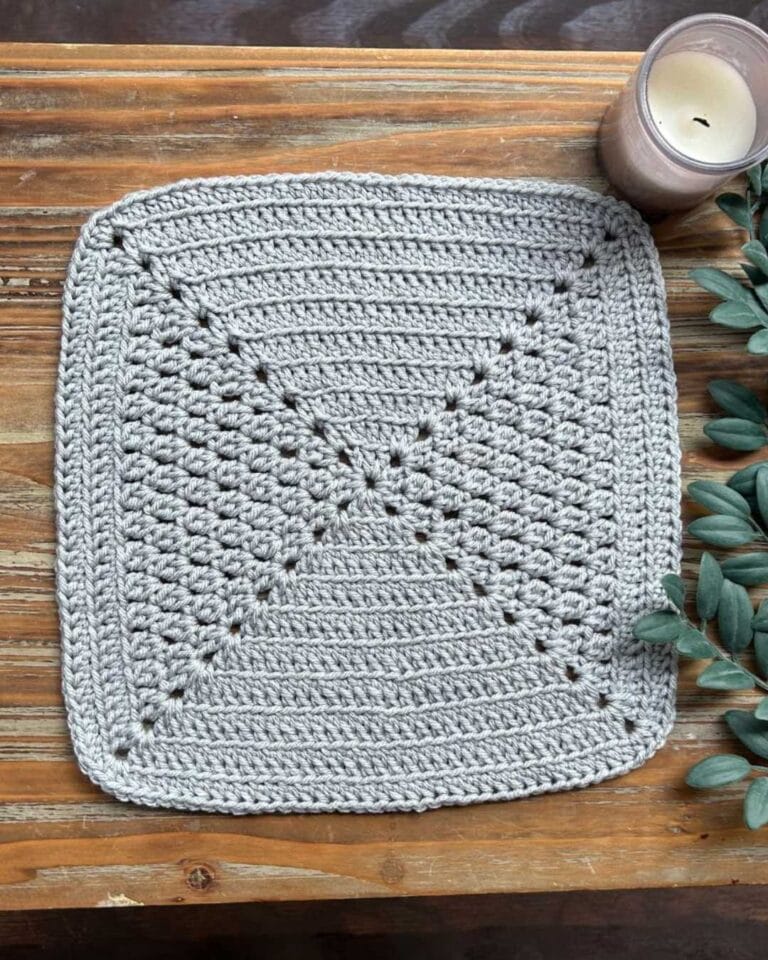 cluster stitch granny square on wooden table with greenery and a candle