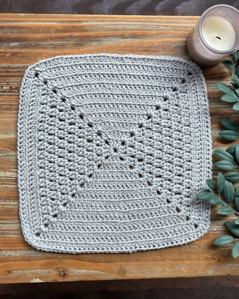 cluster stitch granny square on wooden table with greenery and a candle