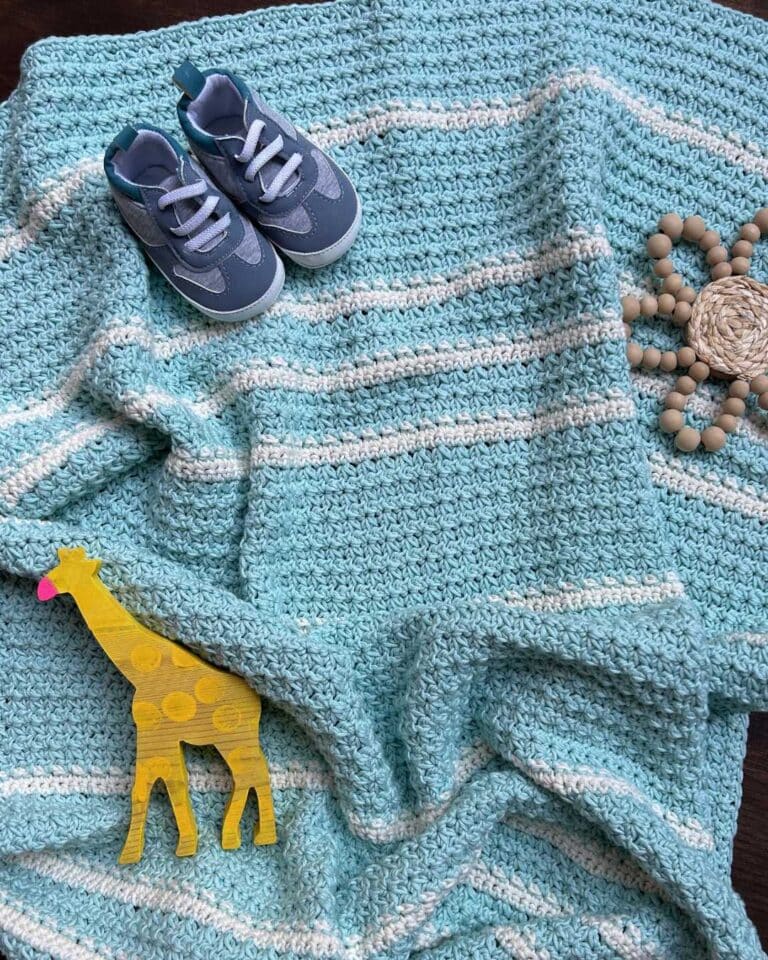 crochet trinity stitch baby blanket with baby shoes and toys