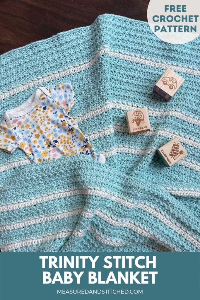 blue and white crochet baby blanket with baby items, text reads "Trinity Stitch Baby Blanket, measuredandstitched.com, free crochet pattern"