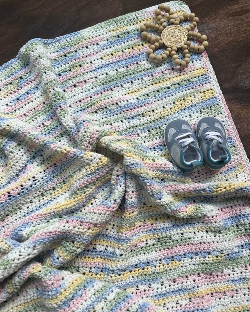 half double crochet shell stitch baby blanket with wooden baby toy and blue baby shoes